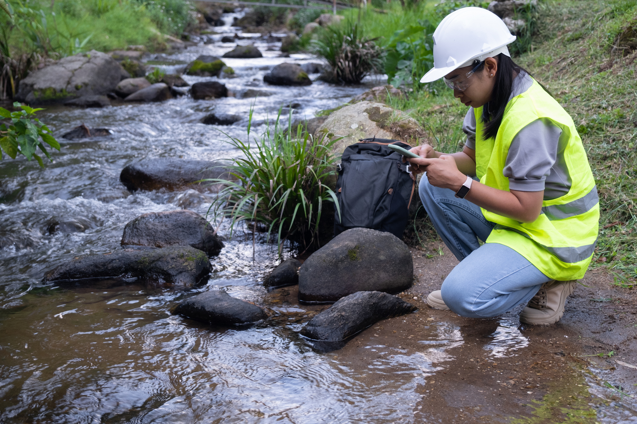 woman taking water sample next to running water river